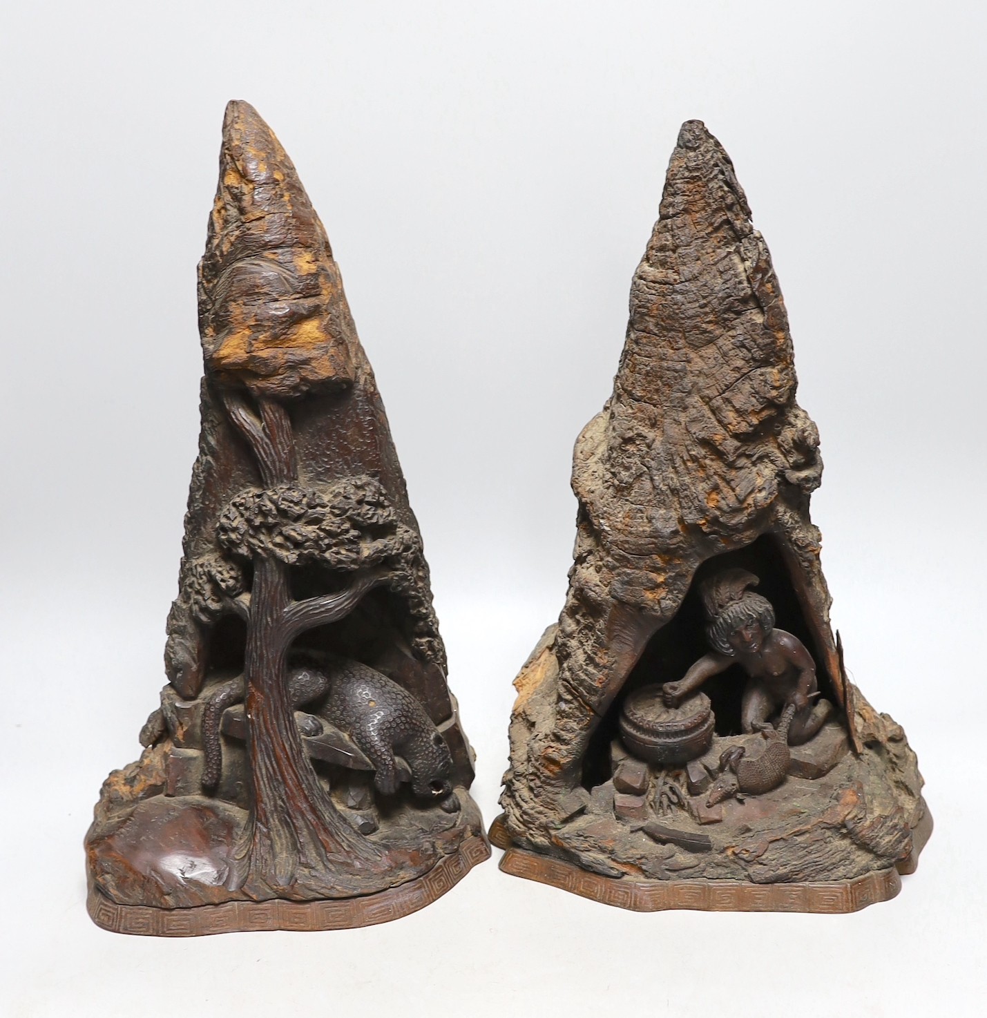 A wood carving of a bear climbing amongst rocks and a tree and another similar carving of figure cooking inside a cave, 40cms high